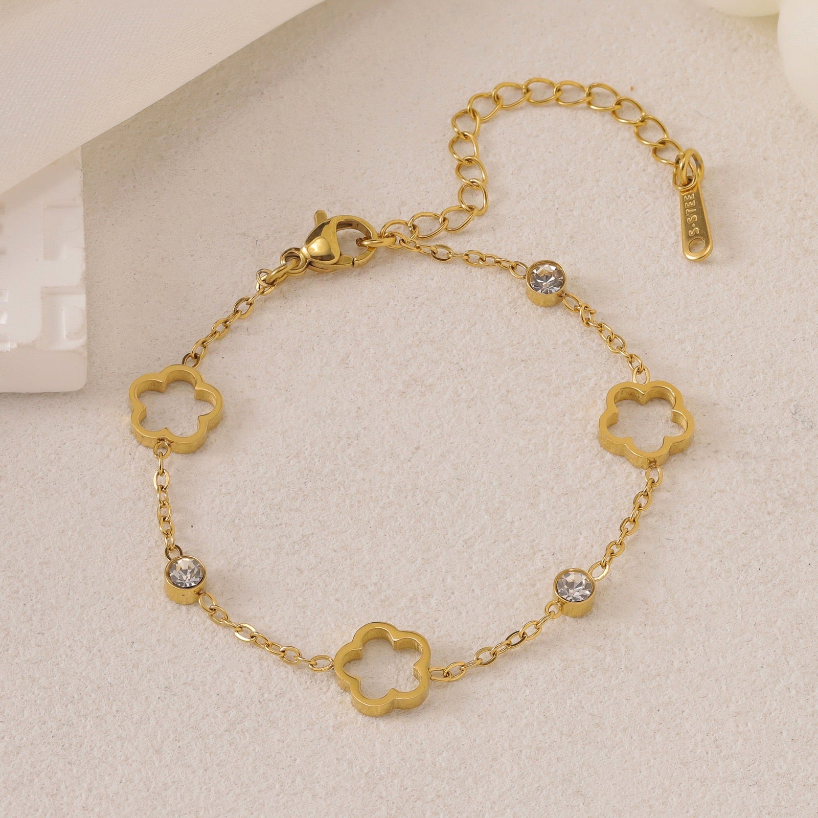 Gold-toned chain bracelet with open clover charms, clear cubic zirconia stones, and an 'S-STEEL' tag.