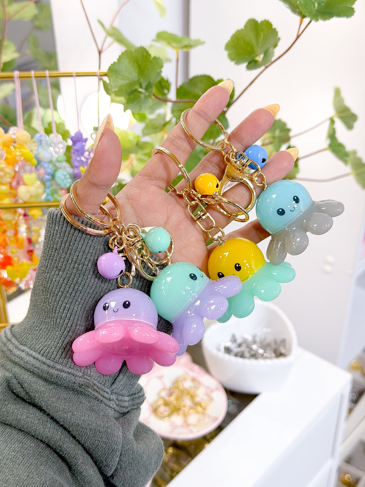 Colorful translucent octopus charms with smiling faces on gold keyrings, held in a hand wearing a green sweater.