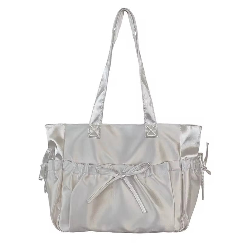 Satin tote bag with bow detailing and tie closures on side pockets.