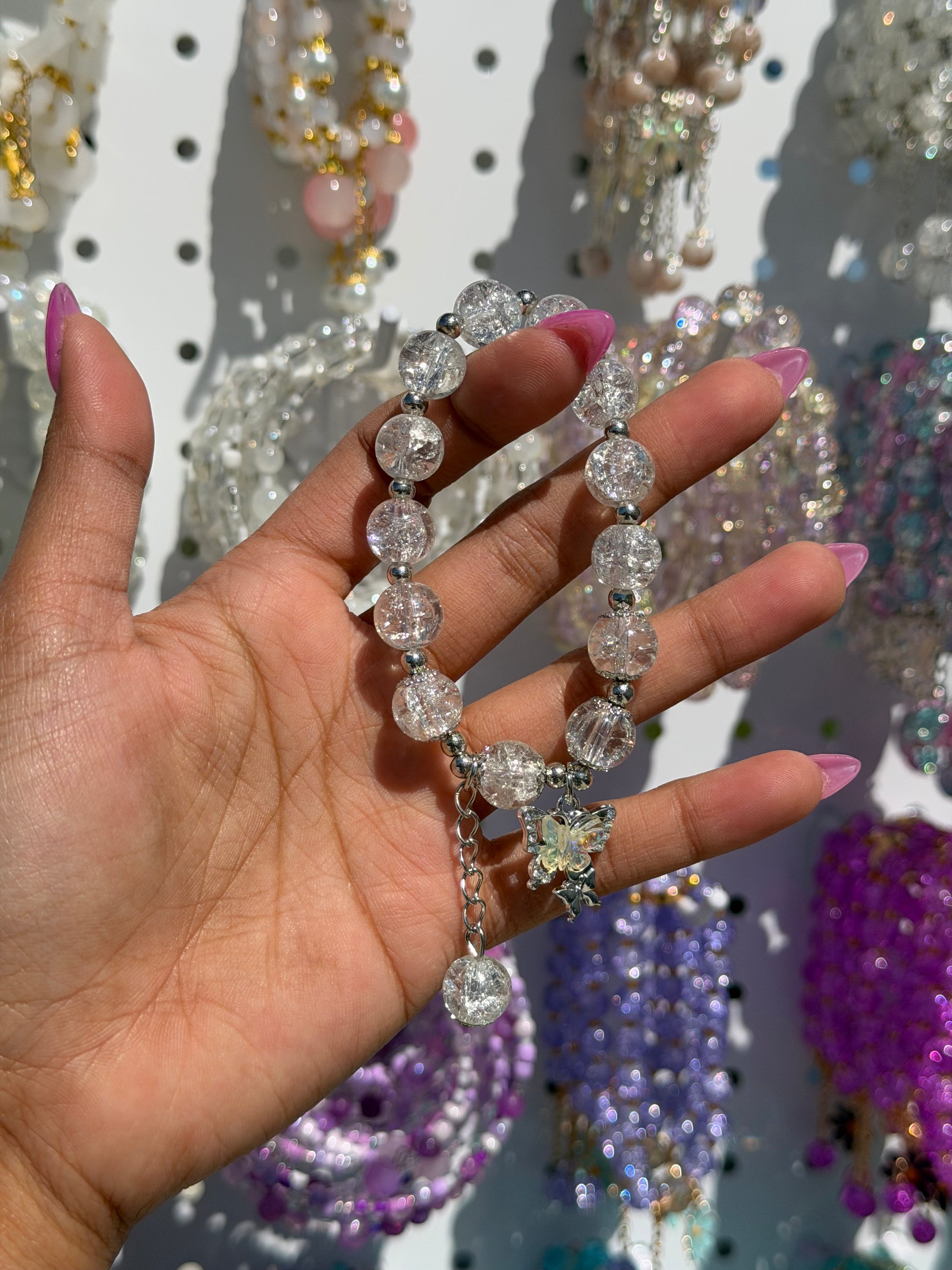 White cracked glass beaded bracelet with silver accents and an iridescent butterfly charm, held in a hand.