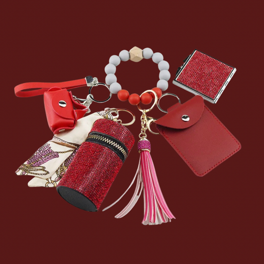 Red Luxe keychain wristlet accessory set featuring a beaded wristlet, rhinestone zip pouch, mini pouch, tassel charm, card holder, and sparkly compact mirror in coordinating colors.