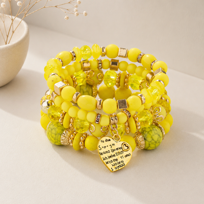 Yellow beaded charm bracelet set with gold-tone accents and heart pendant featuring multilingual love inscriptions, stacked and displayed on a neutral surface.
