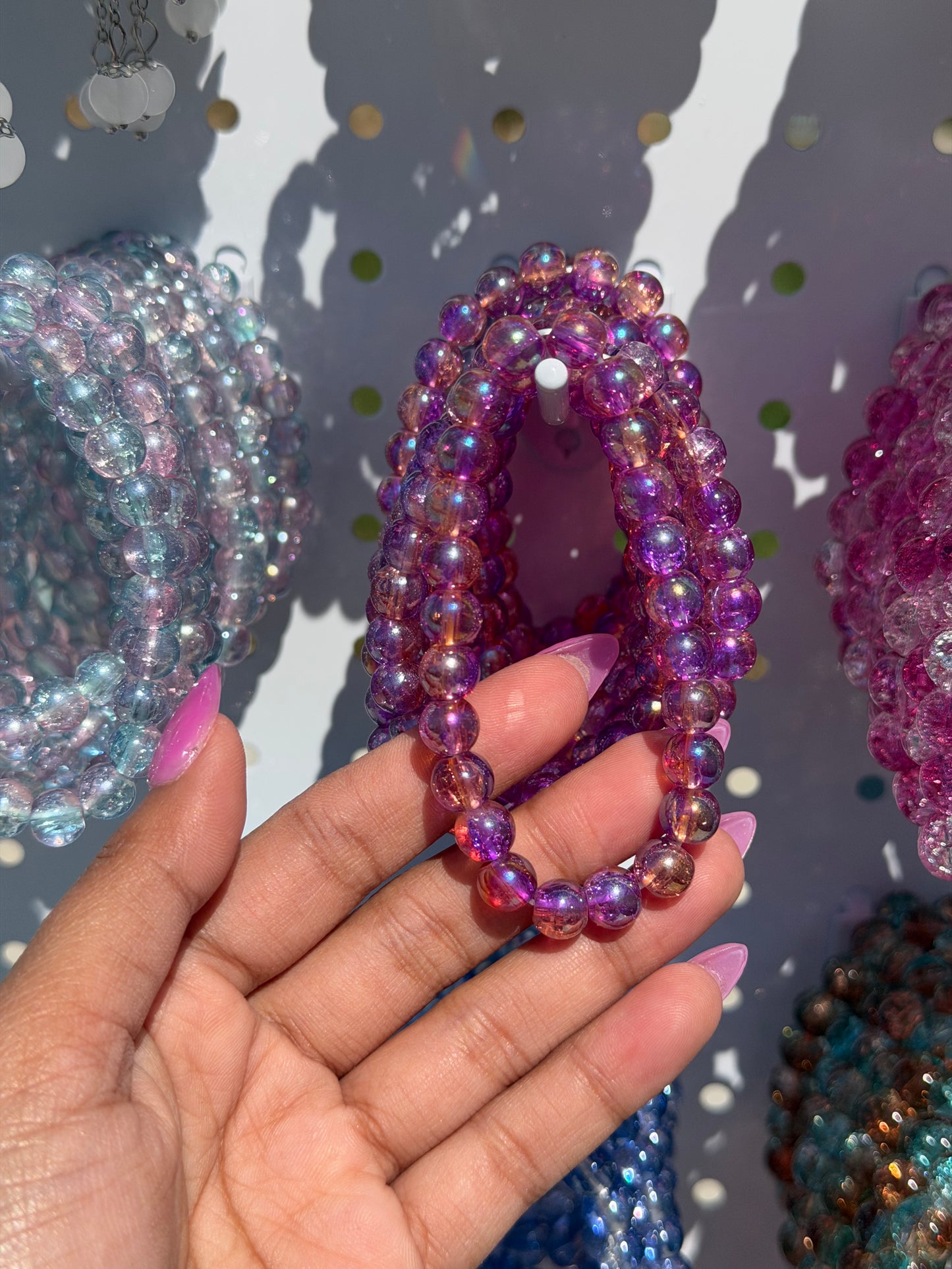 Lilac beaded bracelet with iridescent finish, held by a hand, among other colorful beaded bracelets.