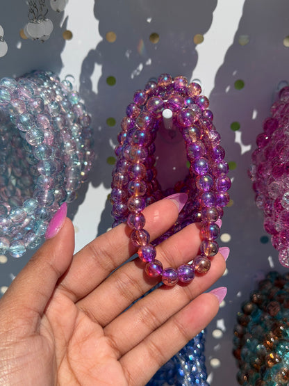 Lilac beaded bracelet with iridescent finish, held by a hand, among other colorful beaded bracelets.