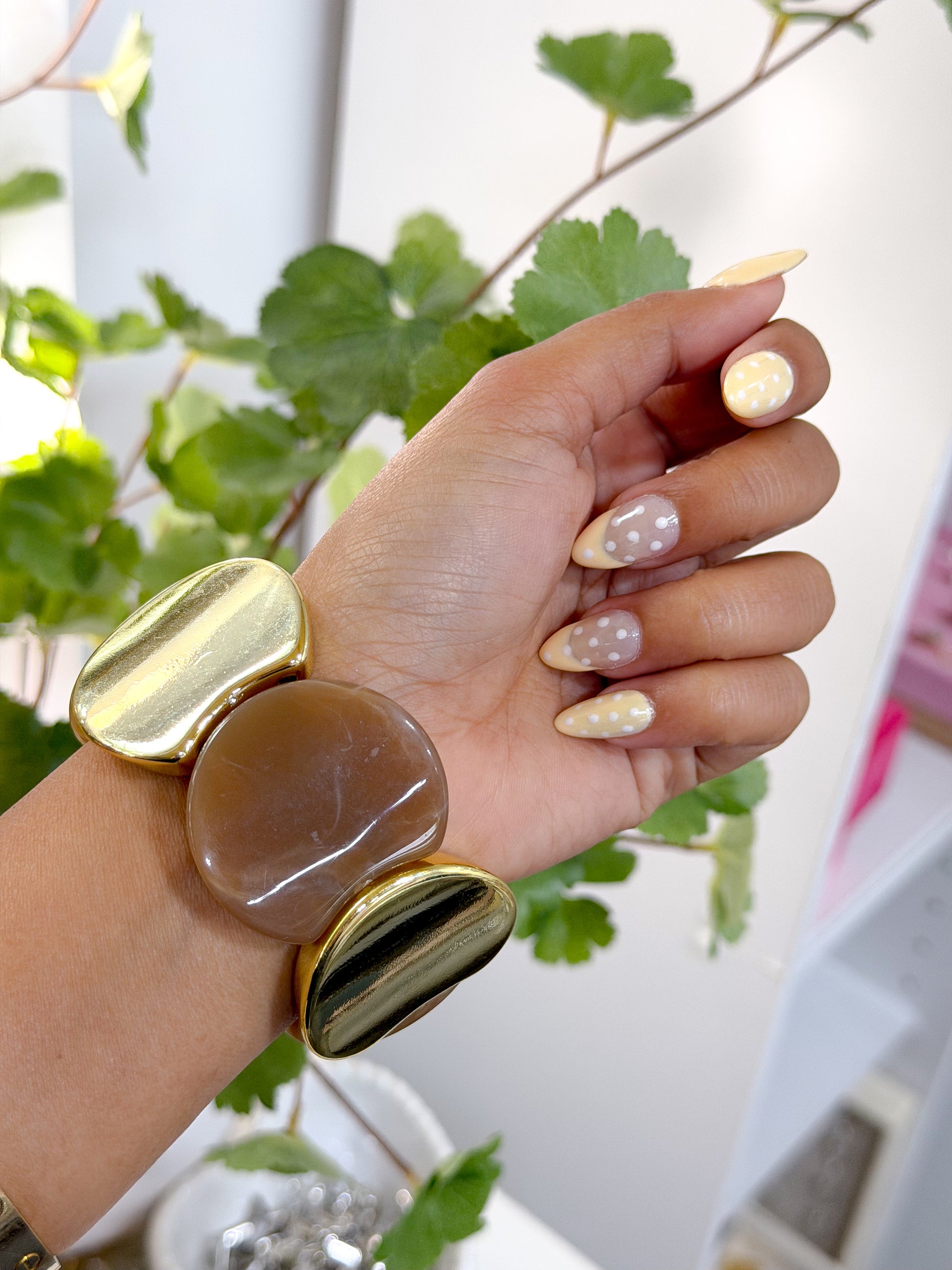 Chunky statement bracelet with polished gold-toned and brown pieces, worn on a wrist with yellow polka dot nails.