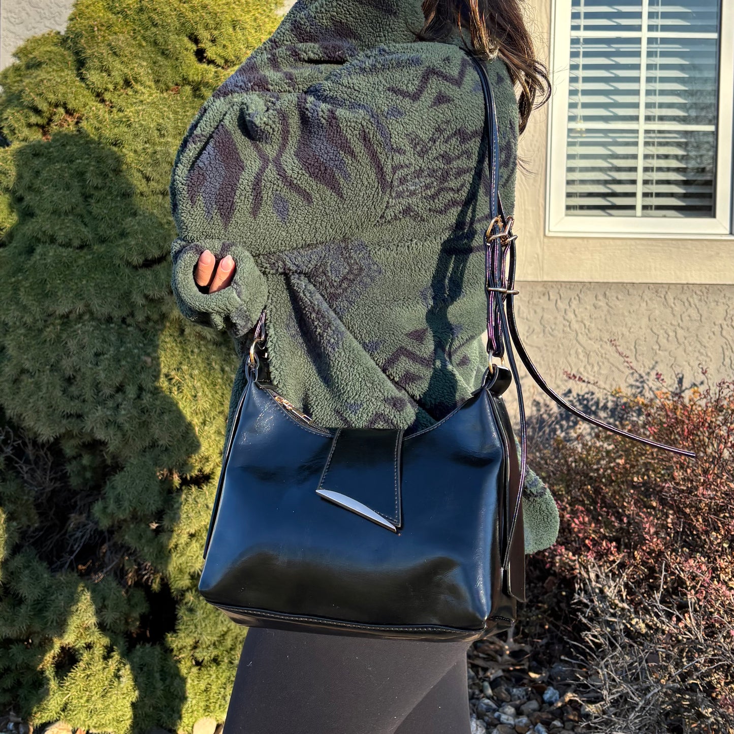 Black shoulder bag with a silver accent, styled with a patterned green fleece jacket and leggings.