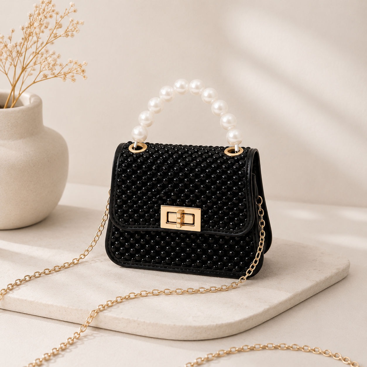 Black beaded mini crossbody bag with pearl top handle and gold chain strap, front view on stone surface