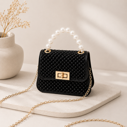 Black beaded mini crossbody bag with pearl top handle and gold chain strap, front view on stone surface