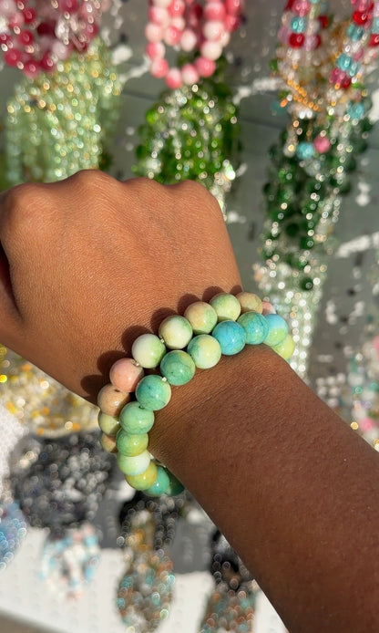 A Green Marble Beaded Bracelet with pastel green, yellow, pink, and blue marbled beads, worn with another on a dark-skinned wrist.