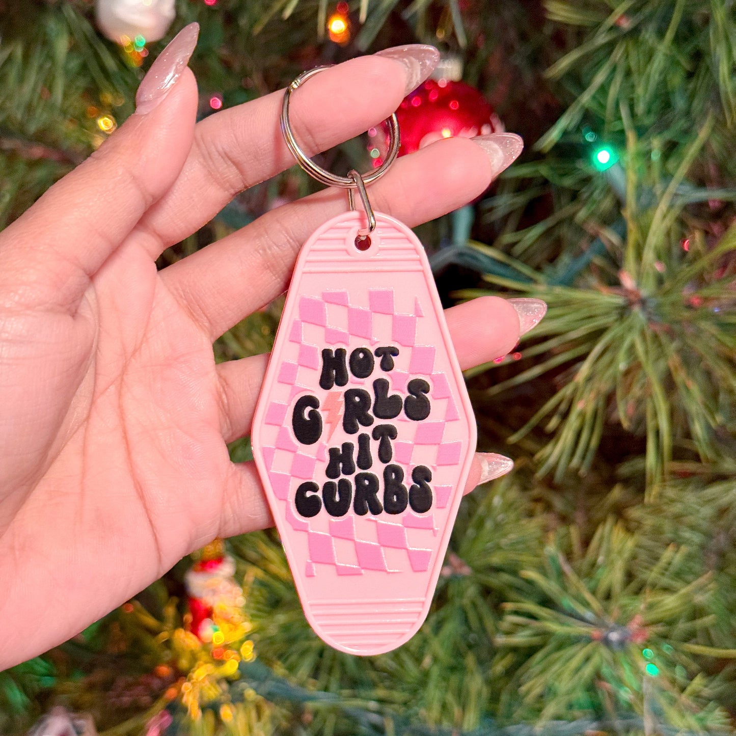 Pink motel keychain by the vendor with checkered pattern and "Hot Girls Hit Curbs" in black.