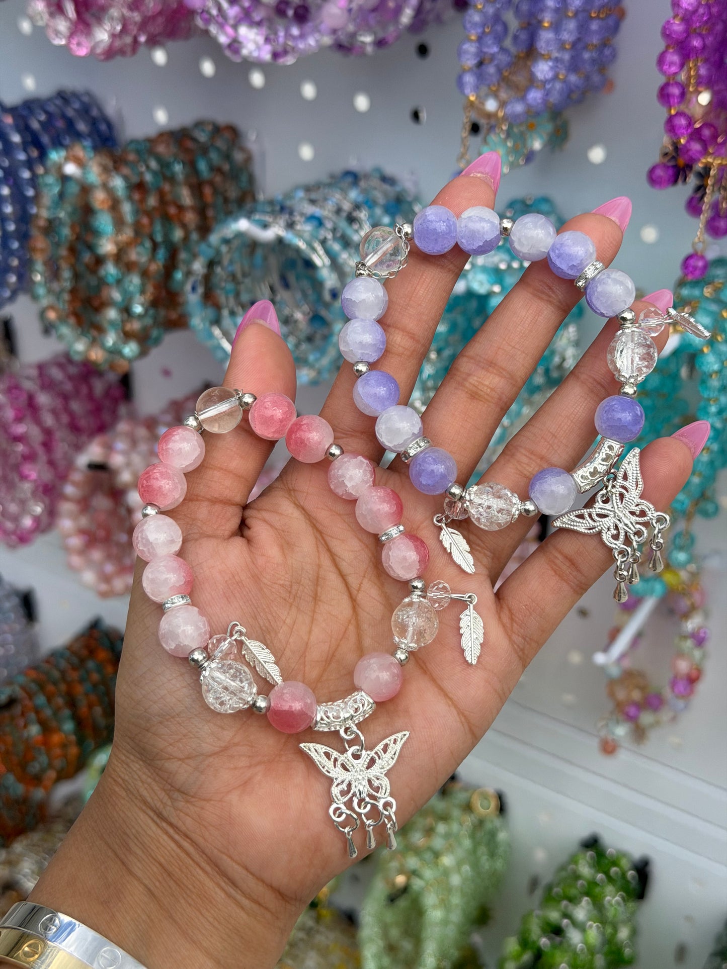 Cracked pink, purple, and clear beaded bracelet with silver butterfly and feather charms, held in a hand.