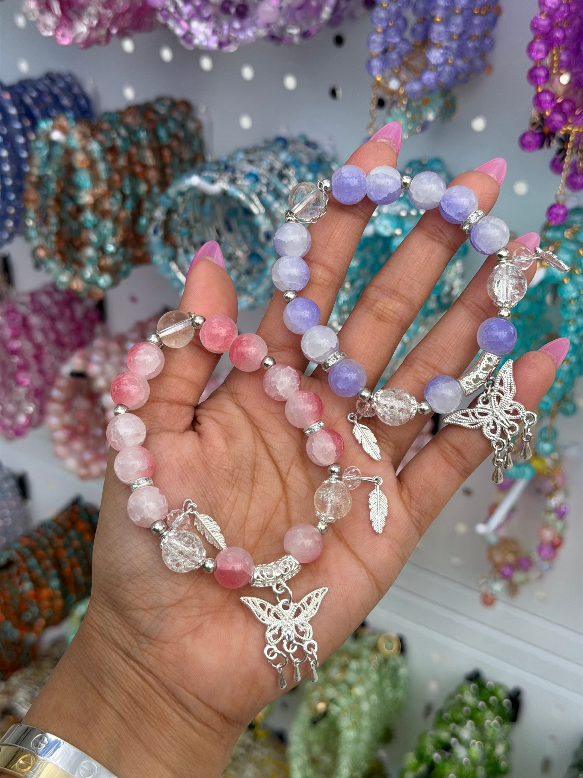 Cracked pink, purple, and clear beaded bracelet with silver butterfly and feather charms, held in a hand.