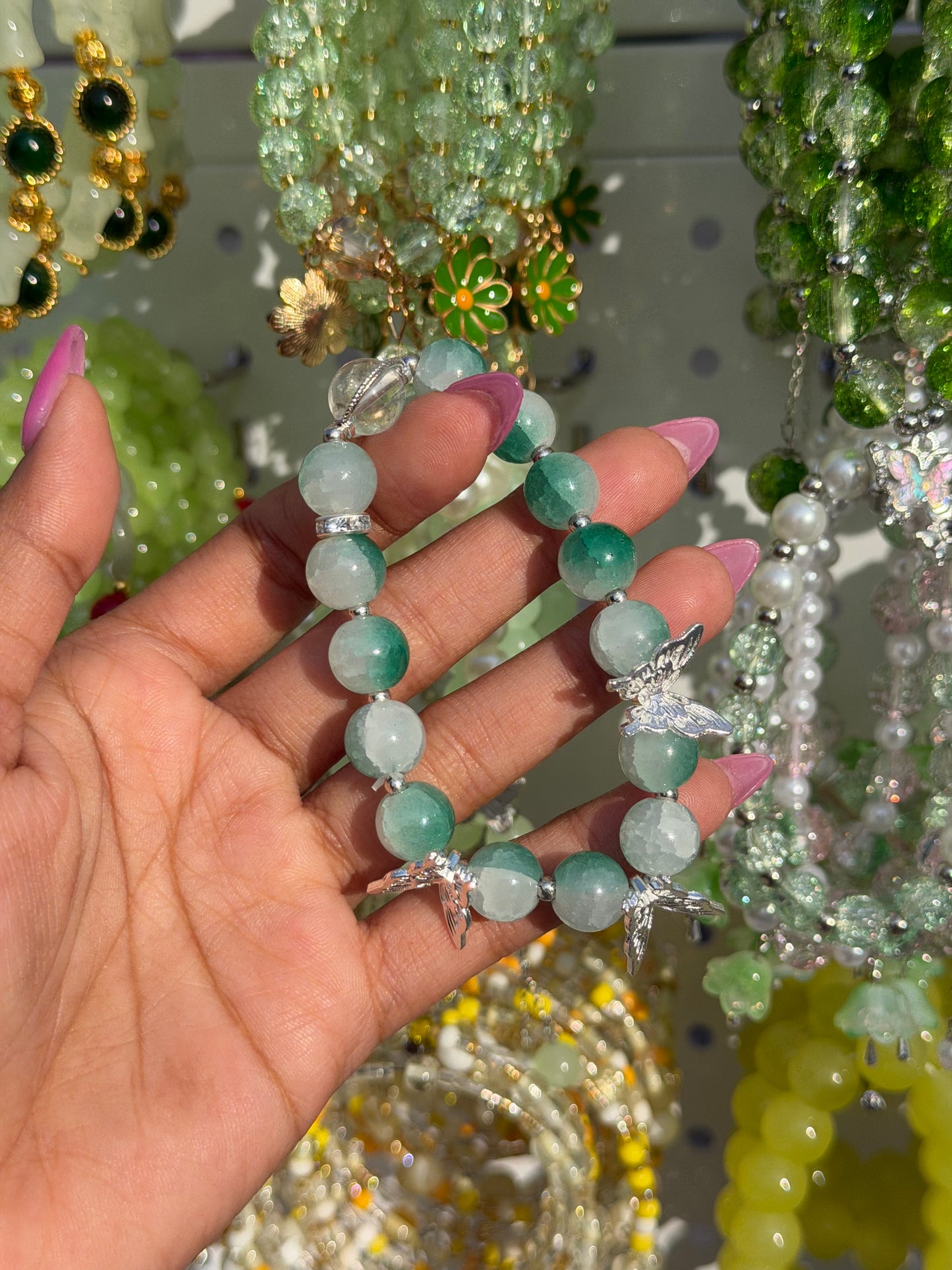 Green beaded bracelet with silver butterfly charms, held by a hand with pink nails.