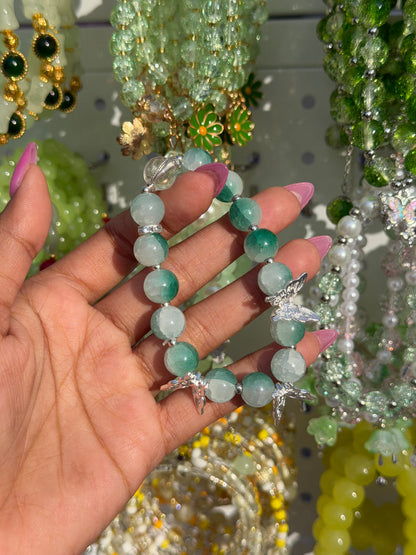 Green beaded bracelet with silver butterfly charms, held by a hand with pink nails.