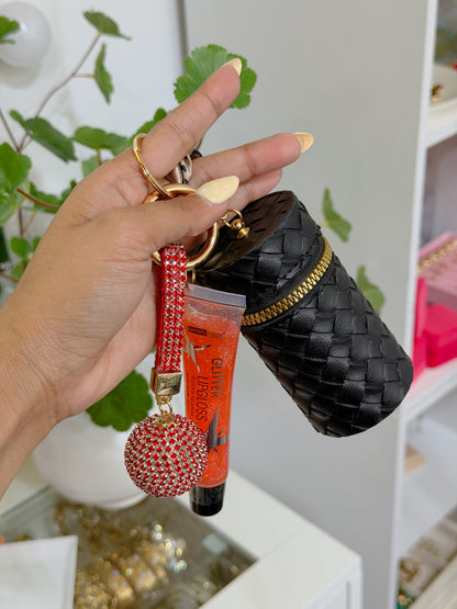 Black woven coin purse with gold zipper, a red rhinestone charm, and an orange glitter lip gloss, held by a hand with yellow polka dot nails.