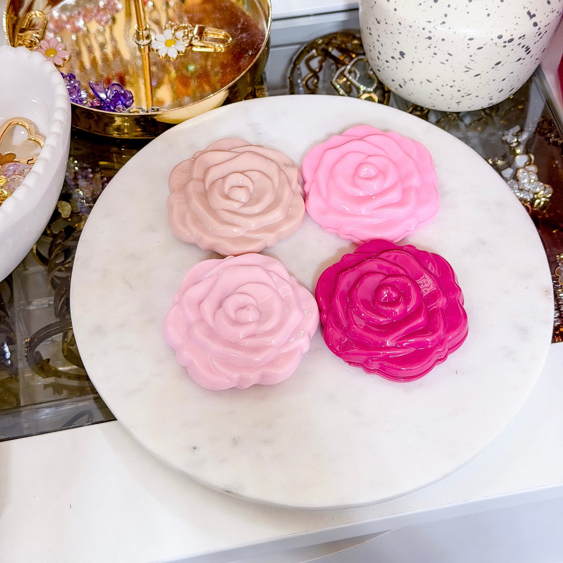 Rose shaped compact mirrors, with varying shades of pink, on a white marble surface.