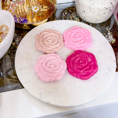 Rose shaped compact mirrors, with varying shades of pink, on a white marble surface.