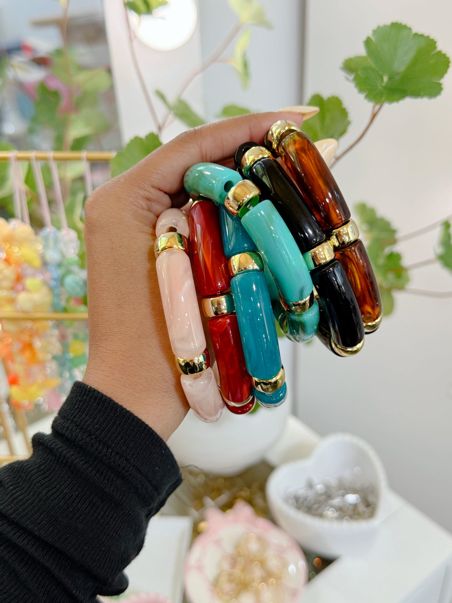 Multi-colored glossy barrel-shaped bracelets with gold accents, stacked and held in a hand.