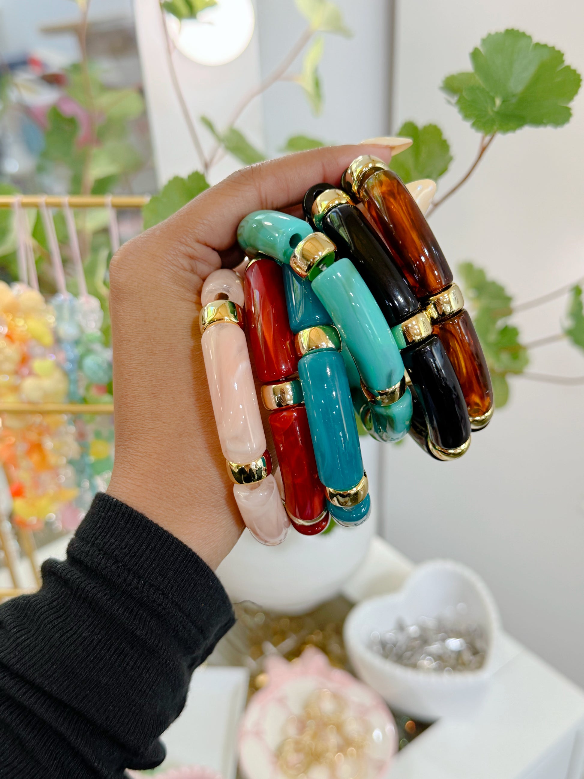 Multi-colored glossy barrel-shaped bracelets with gold accents, stacked and held in a hand.