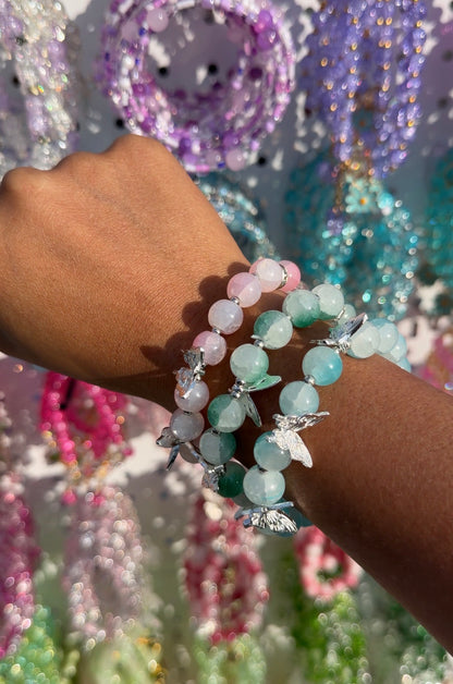 Beaded bracelets with silver butterfly charms in pastel pink, green, and blue, worn stacked on a wrist.