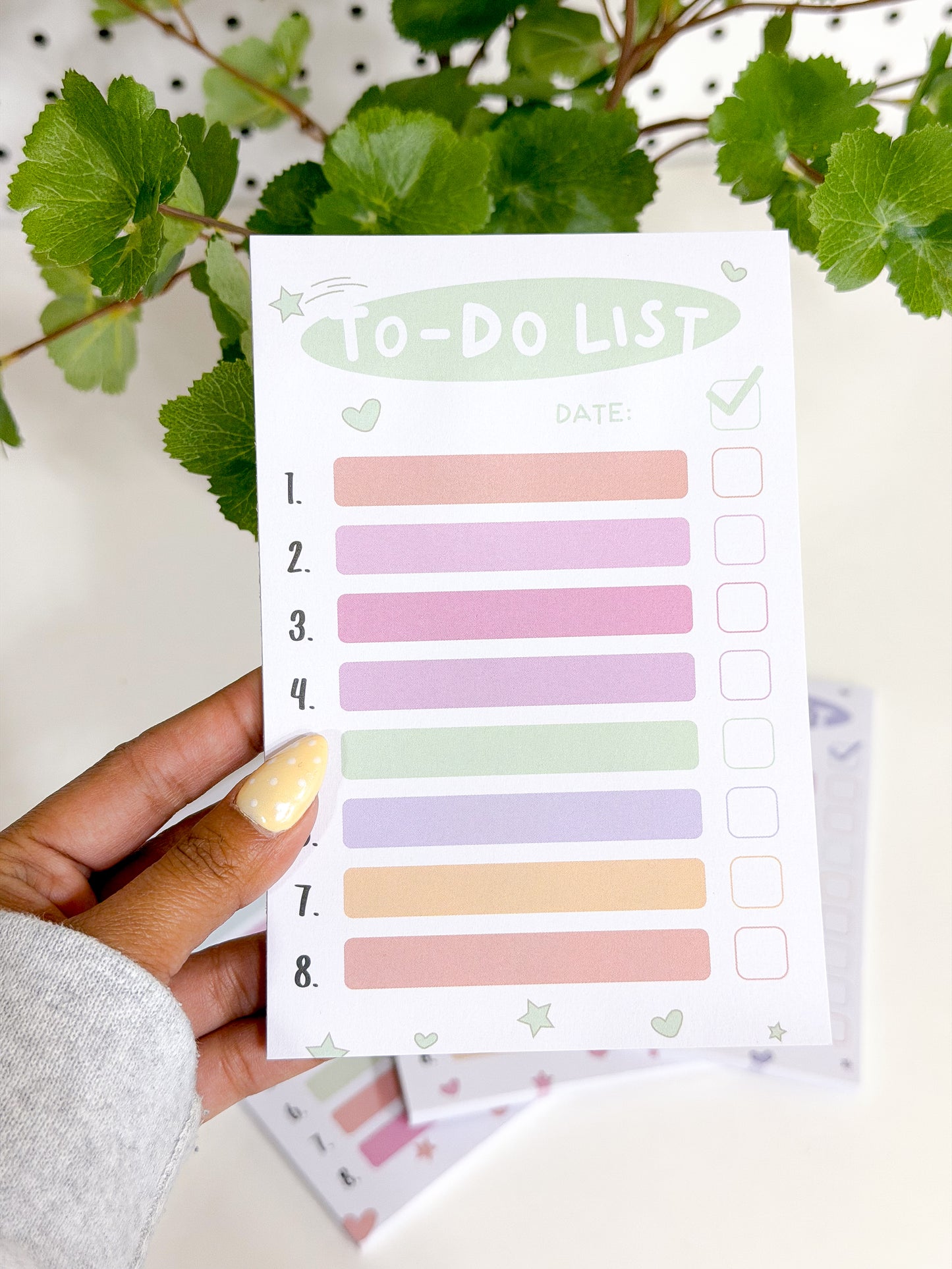 White Tasks Notepad with pastel lines, 'TO-DO LIST' header, and checkboxes, held by a hand with yellow polka dot nail polish.
