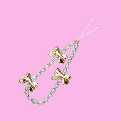 Coquette clear and gold-toned beaded phone charm with three shiny golden bow pendants on a pink background.