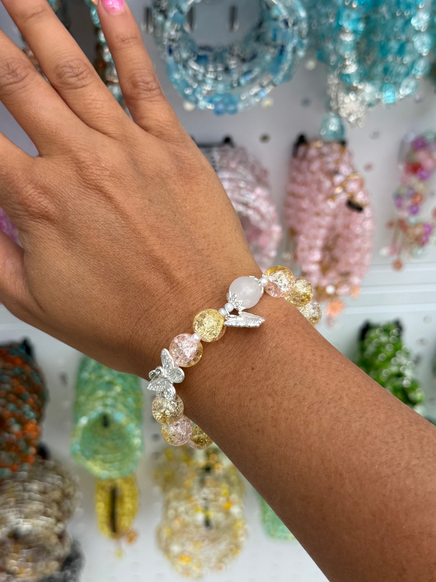 Yellow Butterfly Beaded Bracelet with yellow and pink crackle glass beads, a white oval bead, and silver butterfly charms, worn on a wrist.
