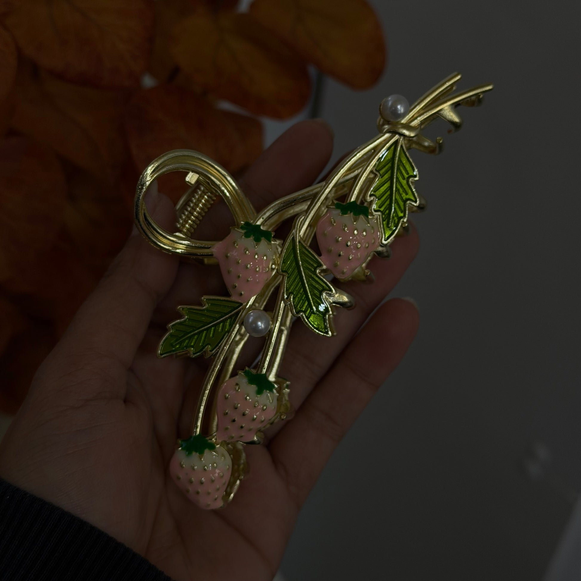 Gold hair claw featuring pink strawberry charms with green leaves, small pearl accents, and a bow-shaped design, photographed on hand