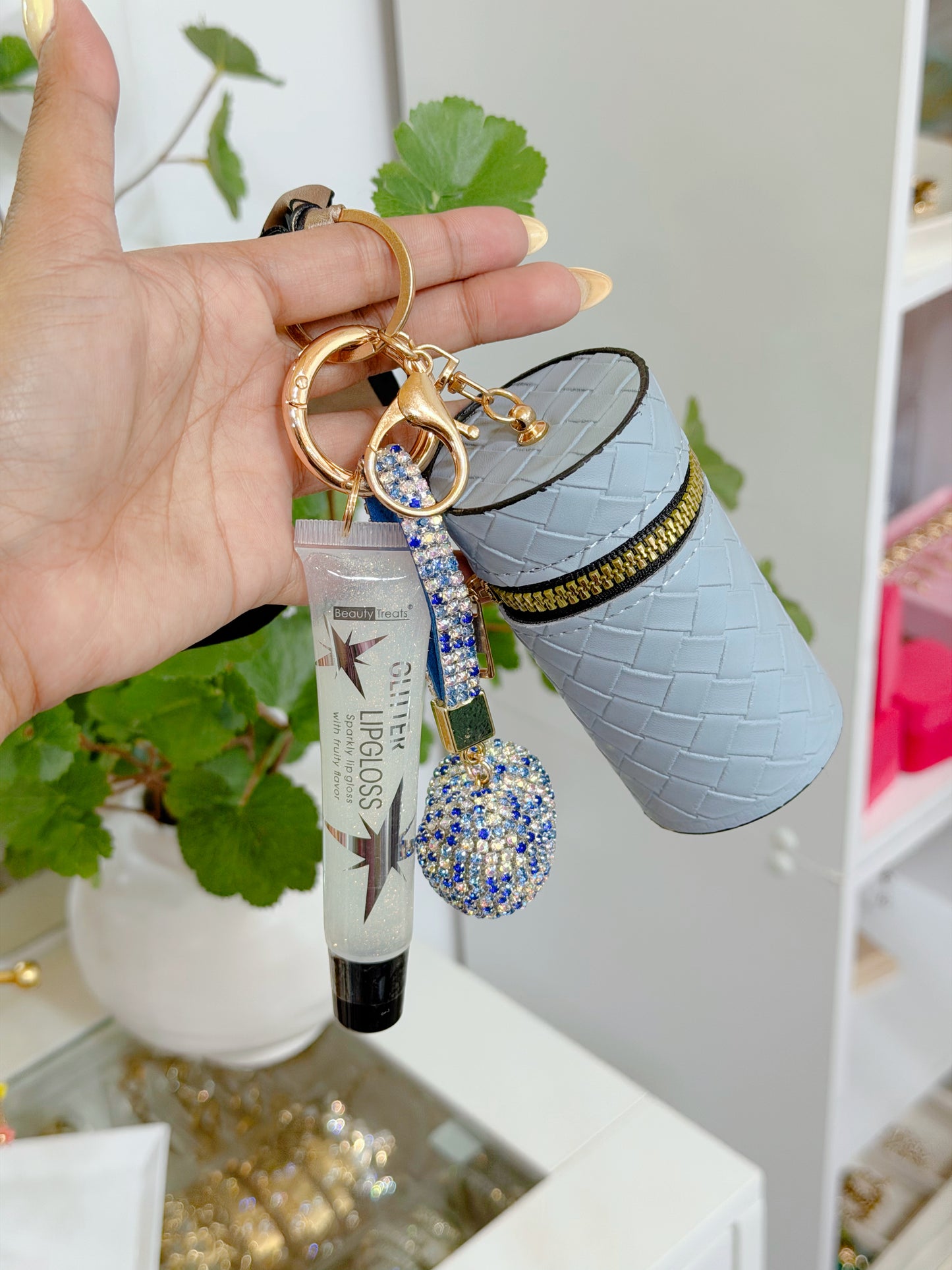 Light blue woven cylindrical coin purse combo set, featuring a clear glitter lip gloss and a blue rhinestone charm, held in a hand.