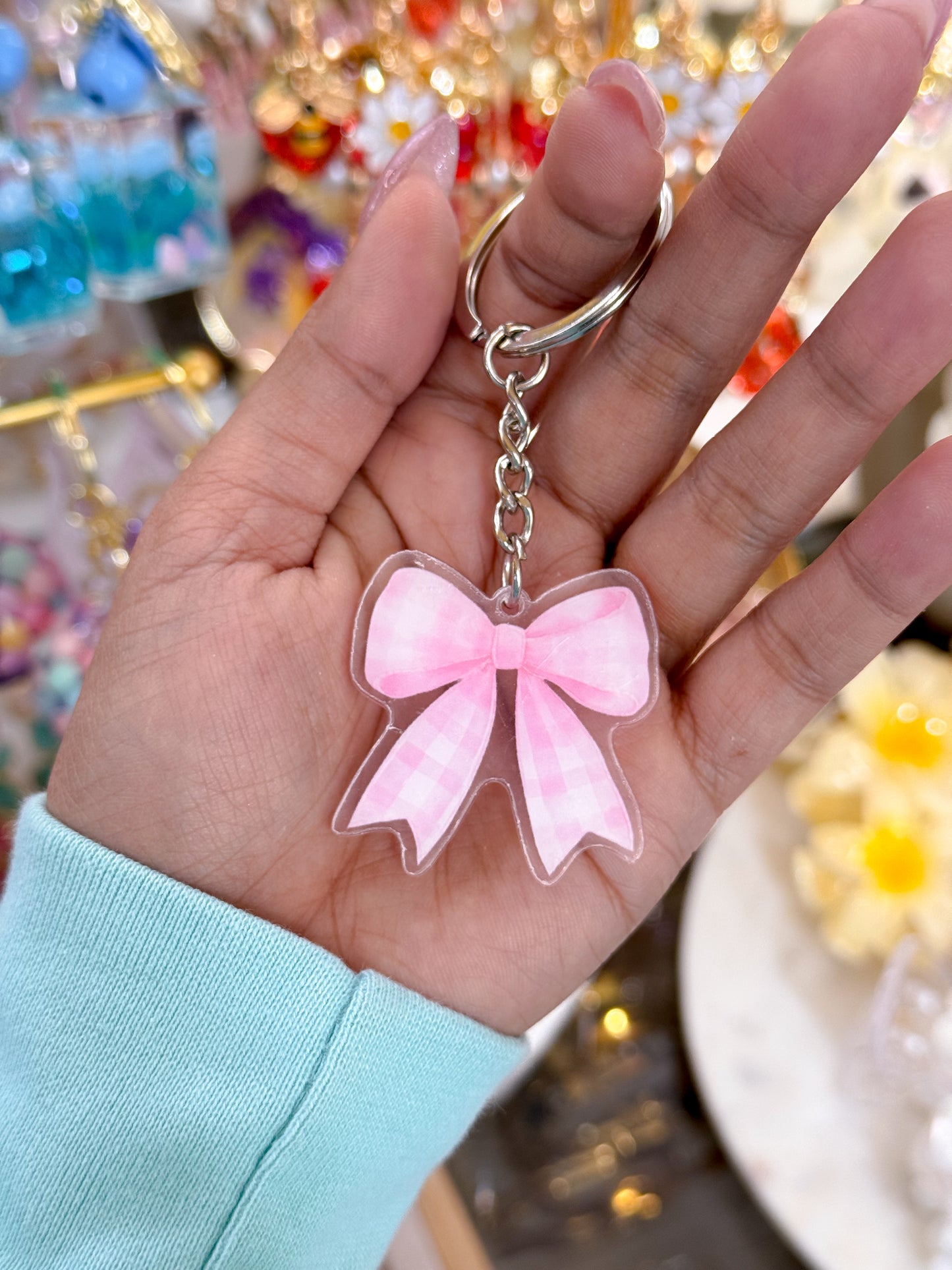 Pink bow keychain with a checkered pattern, from an unknown brand, held in someone's hand.