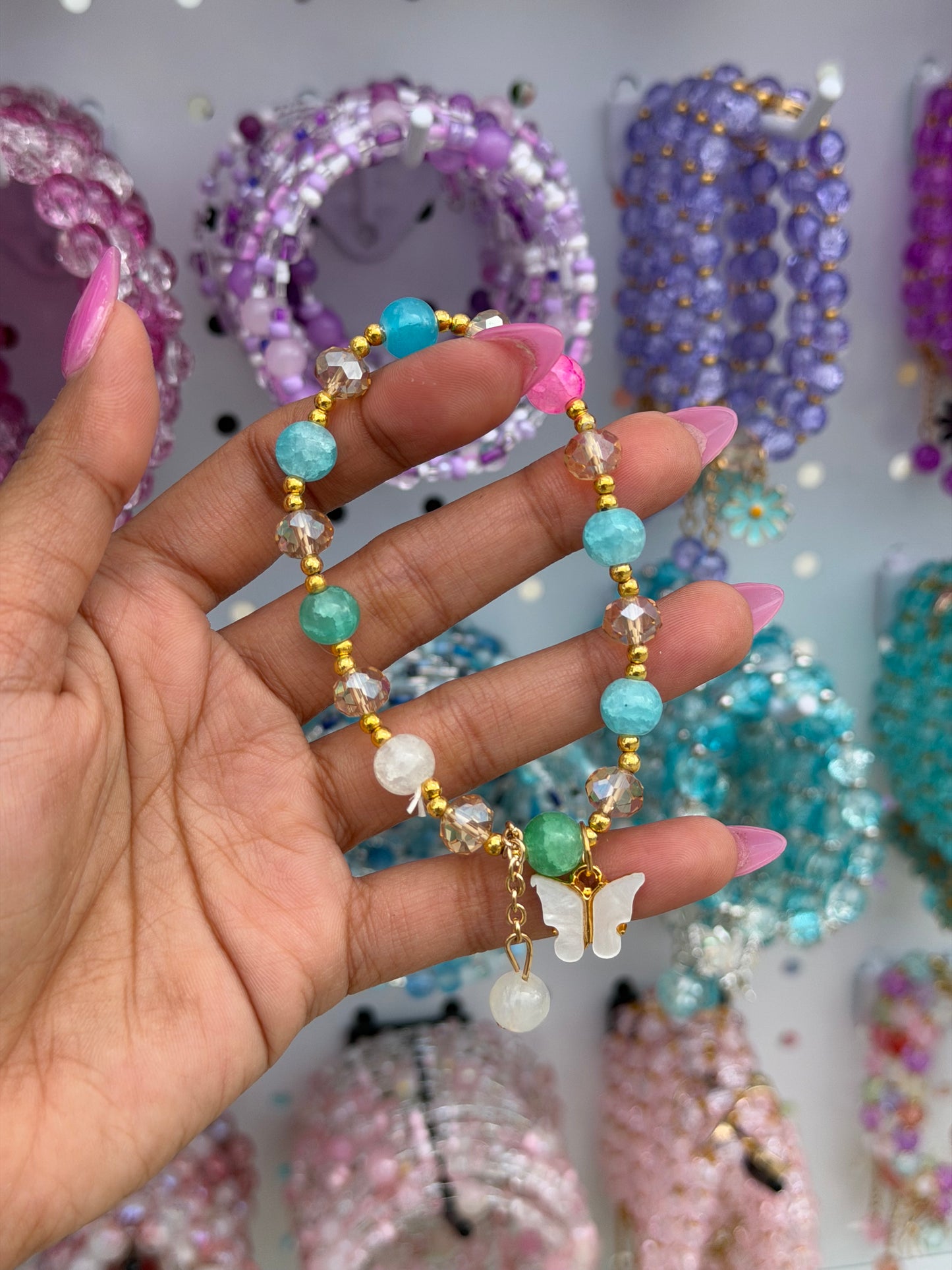 Multi-color crystal butterfly beaded bracelet featuring turquoise, pink, green, and clear beads with a white butterfly charm, held by a hand.