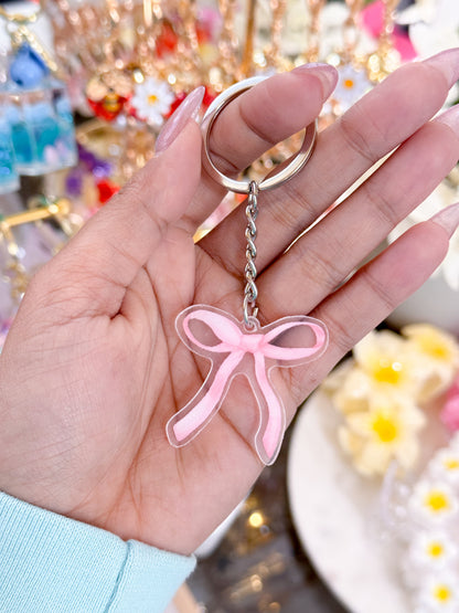 Pink bow keychain with silver hardware and chain, held in hand with long nails.