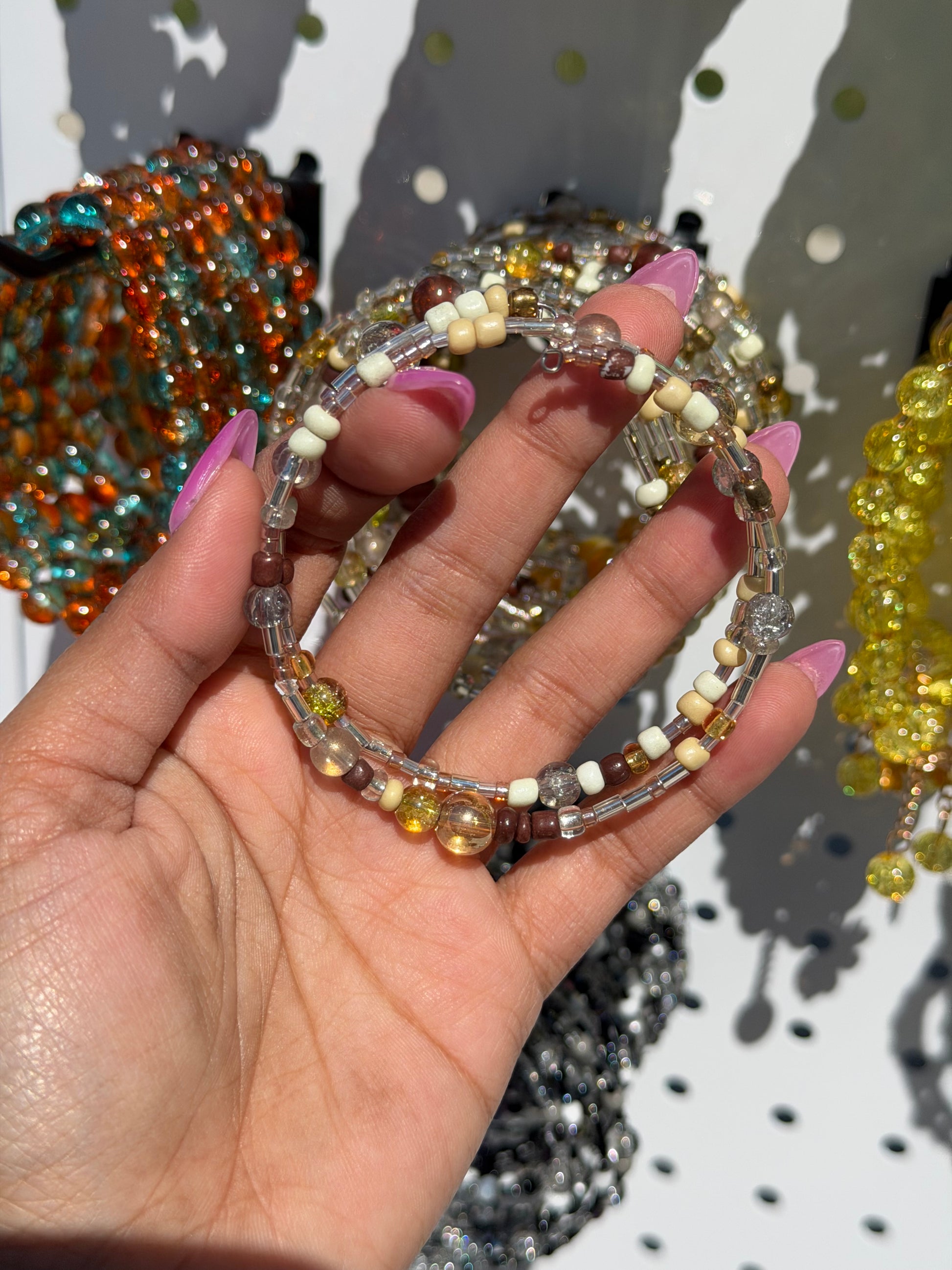 Layered Beaded Bracelets with brown, cream, yellow, and clear beads, held by a hand with pink nails.