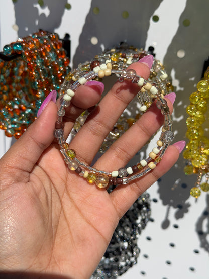 Layered Beaded Bracelets with brown, cream, yellow, and clear beads, held by a hand with pink nails.
