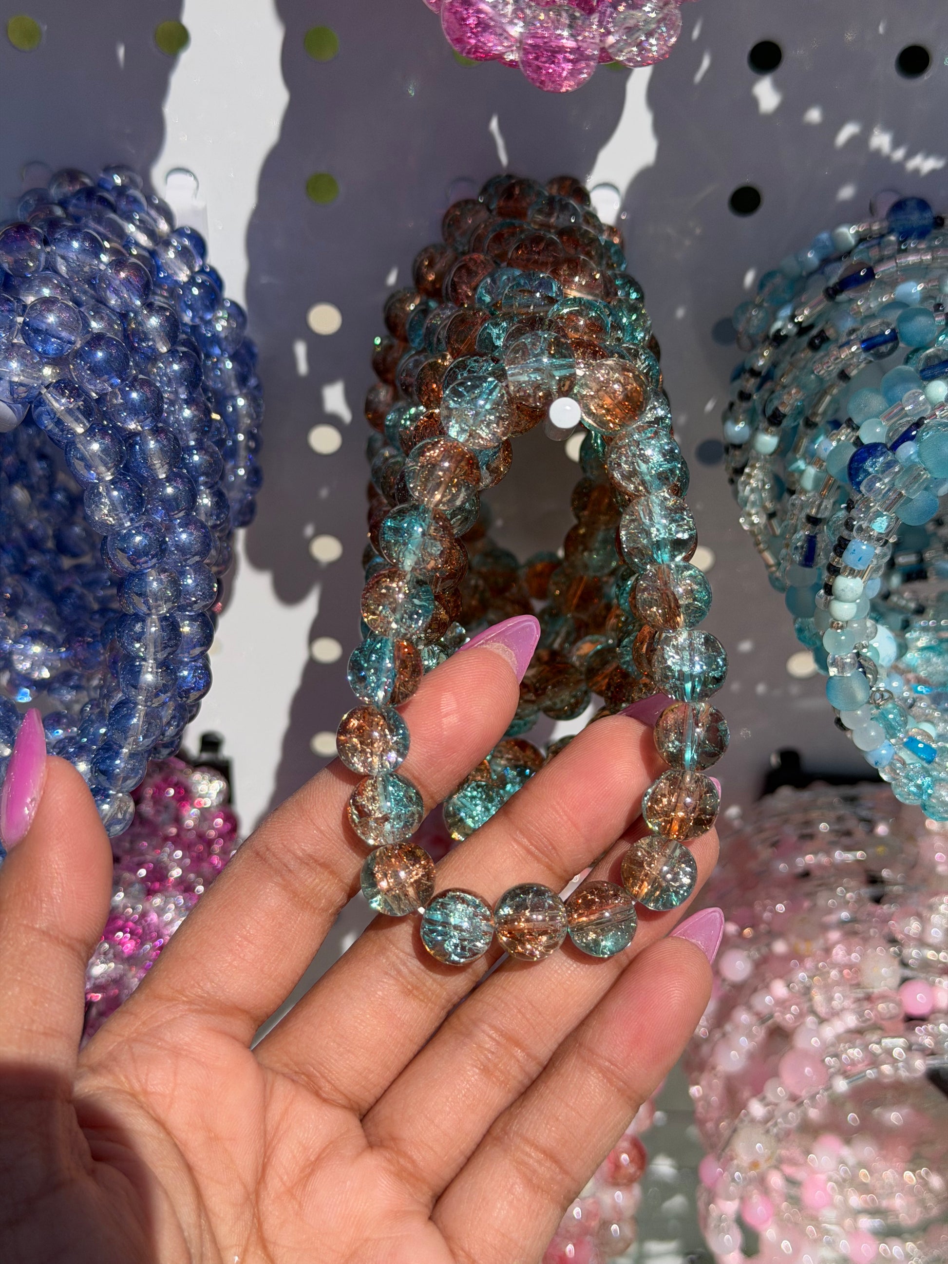Variety of blue beaded bracelets and other colorful styles, with a hand holding a teal and amber crackled glass bracelet.