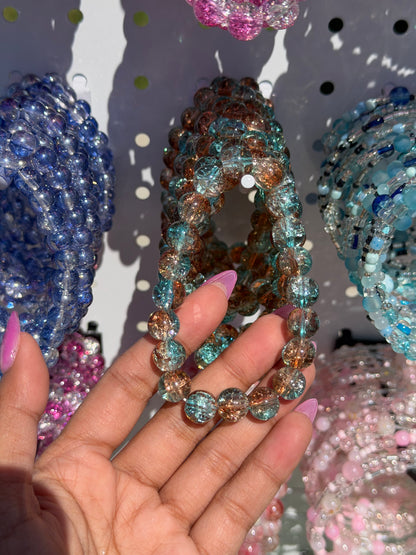 Variety of blue beaded bracelets and other colorful styles, with a hand holding a teal and amber crackled glass bracelet.