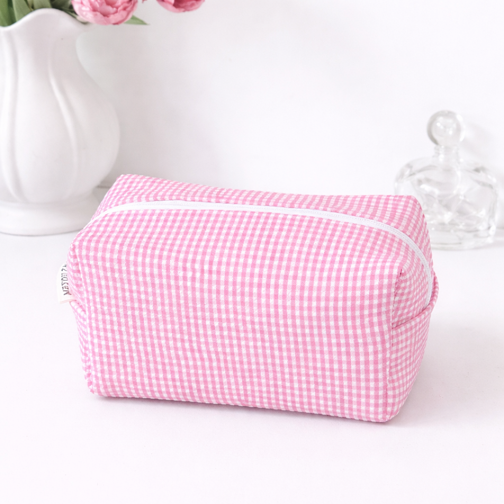 Pink gingham makeup bag with a white zipper and a small white fabric tag on the left side.