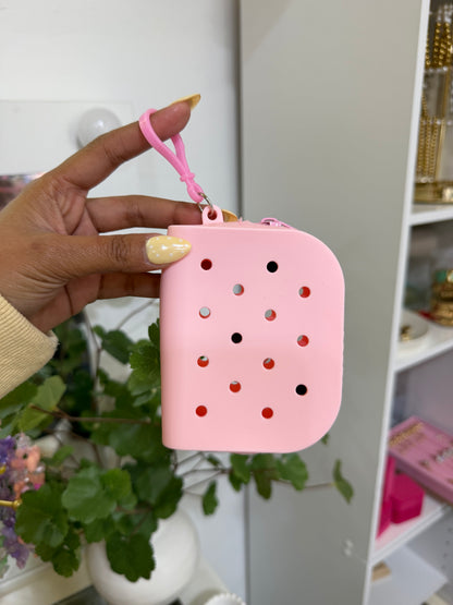 Pink silicone charm pouch with various holes and a top clip, held by a hand with yellow polka dot nails.