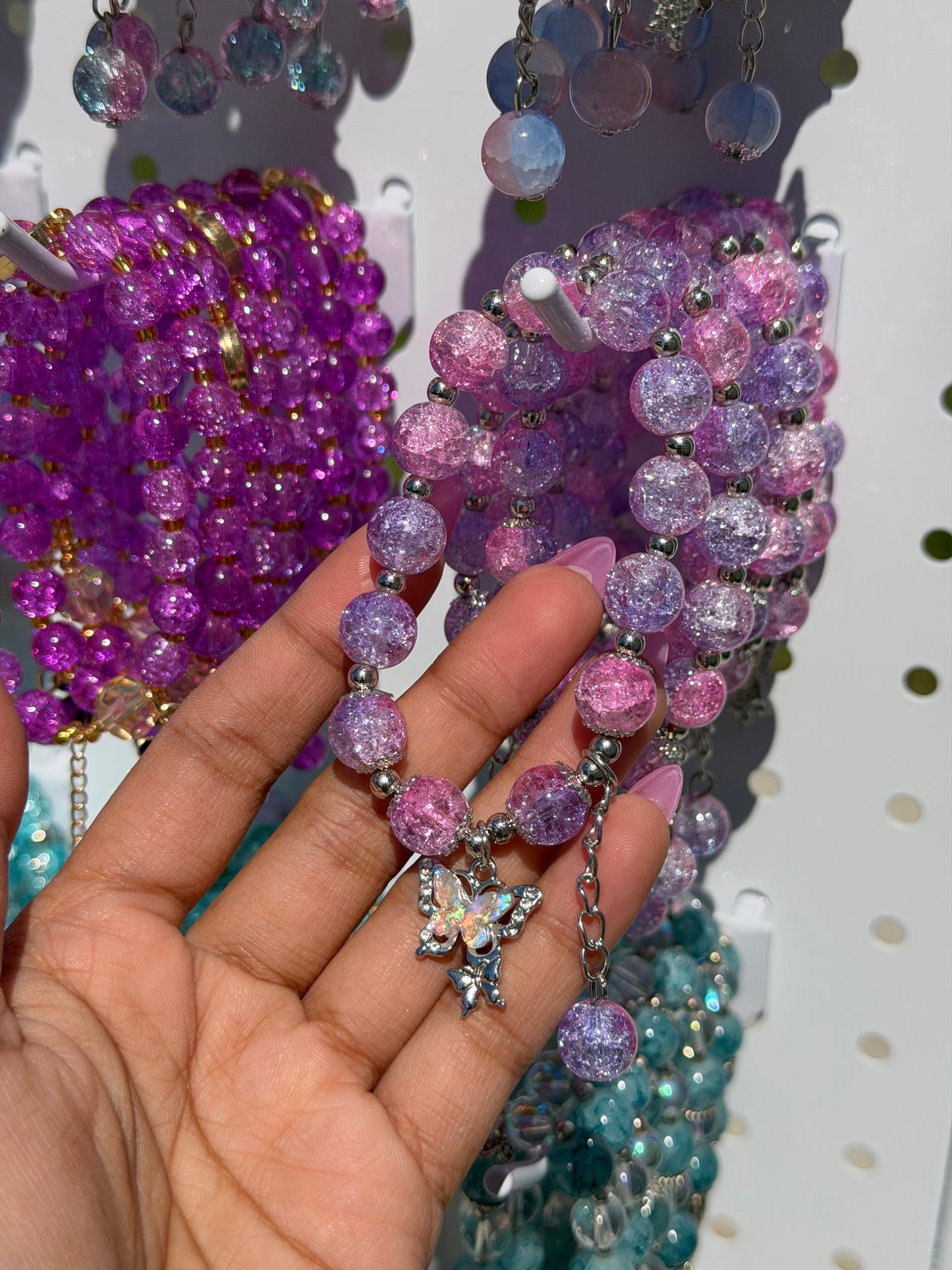 Lilac beaded bracelets with crackle pink and purple beads, silver spacers, and a sparkling butterfly charm, held by a hand.