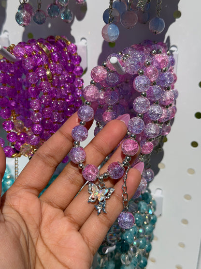 Lilac beaded bracelets with crackle pink and purple beads, silver spacers, and a sparkling butterfly charm, held by a hand.