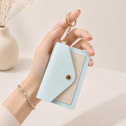Light blue snap card holder with beige interior and gold-tone chain, held in hand, side view, textured surface, minimalist design