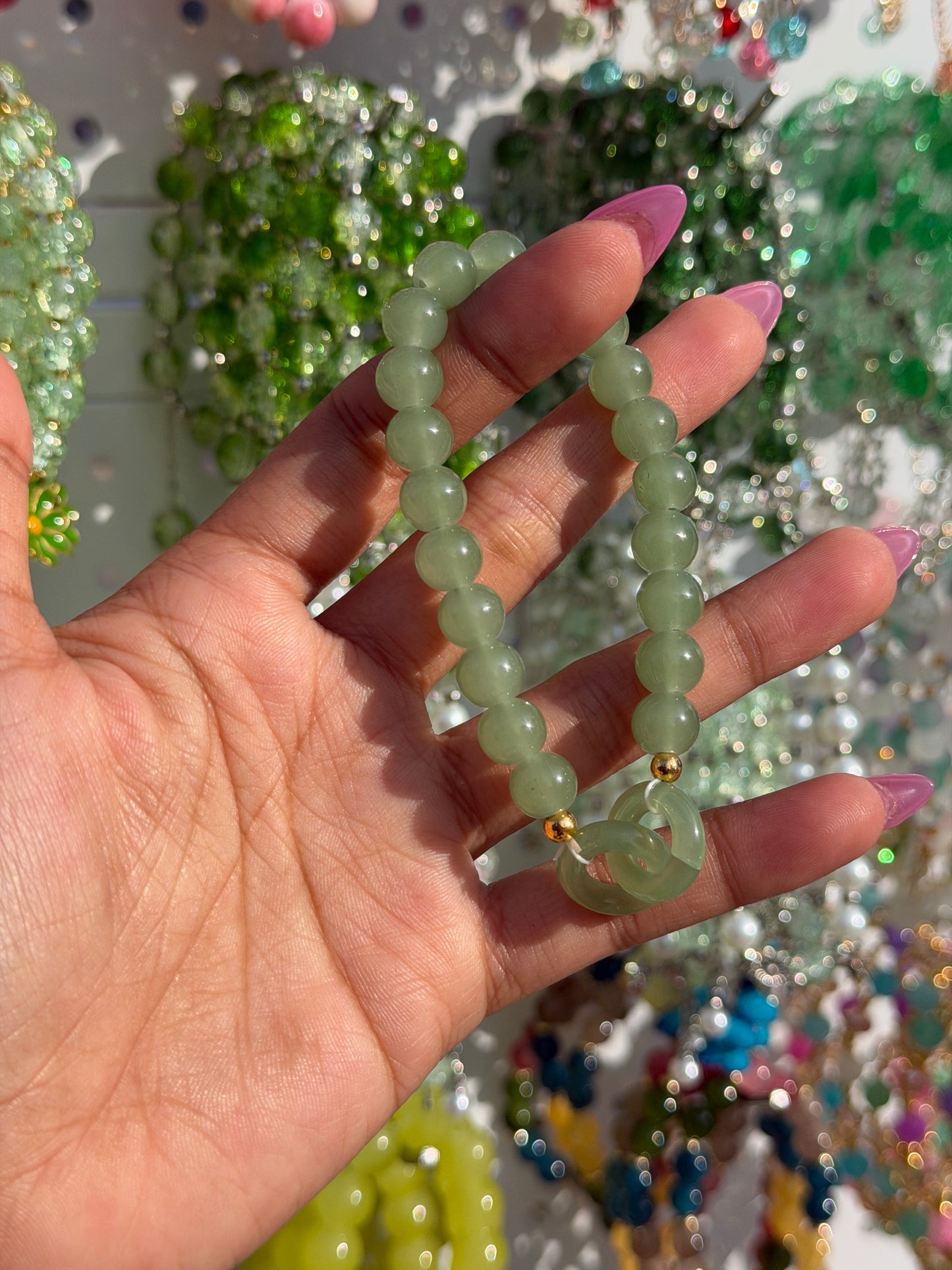 Green Lucky Charms Beaded Bracelet with a gold accent bead and circular charm, held in a hand with pink nails.