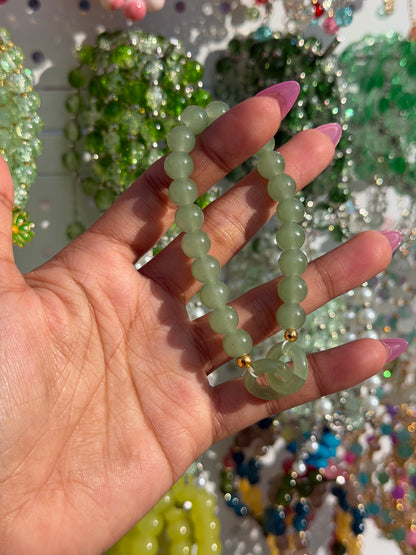 Green Lucky Charms Beaded Bracelet with a gold accent bead and circular charm, held in a hand with pink nails.