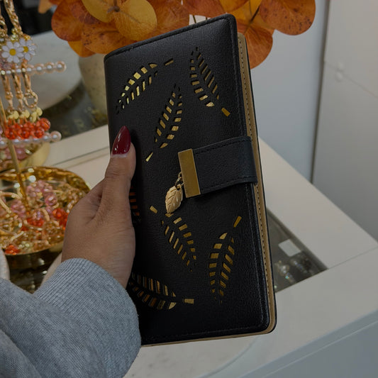 Black wallet with gold detailing held by a hand, with decorative items in the background