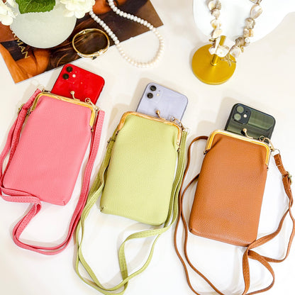 Three slim phone crossbody bags laid flat on a white surface in pink, light green, and tan, each with a gold clasp frame and long strap, shown holding smartphones partially inside.