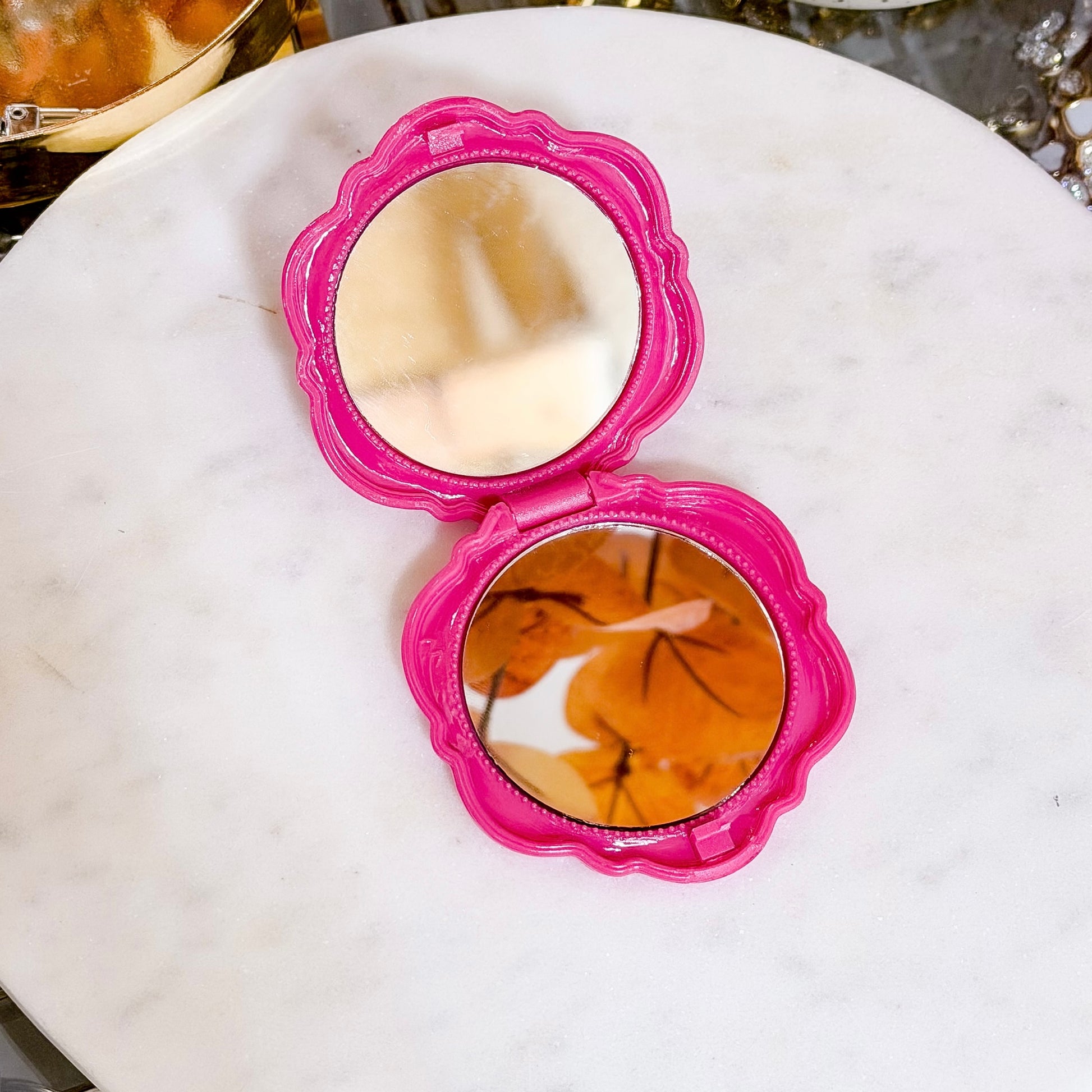 Pink compact mirror with floral trim, open on a marble surface.