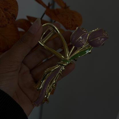 Gold bow-shaped hair claw with purple tulip flowers and green enamel leaves, featuring a smooth glossy finish.