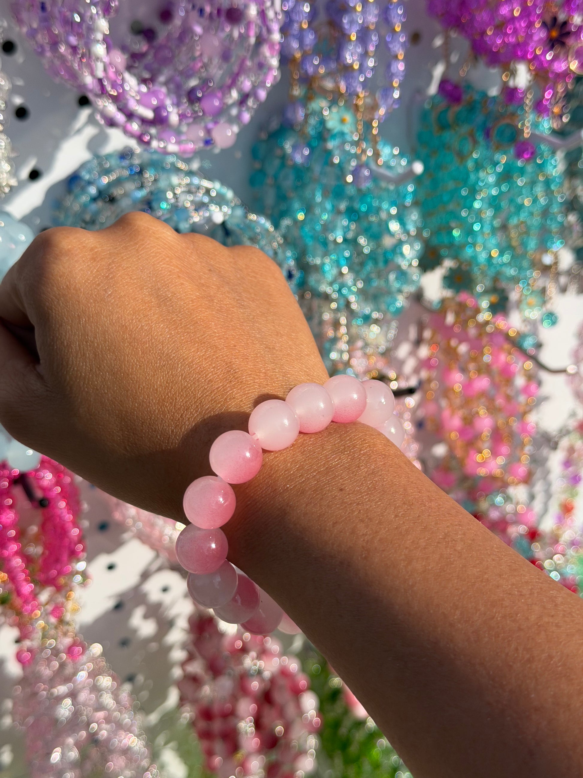Pink Beaded Bracelet with large, round, polished pink beads on a person's wrist, against a blurred background of colorful beads.
