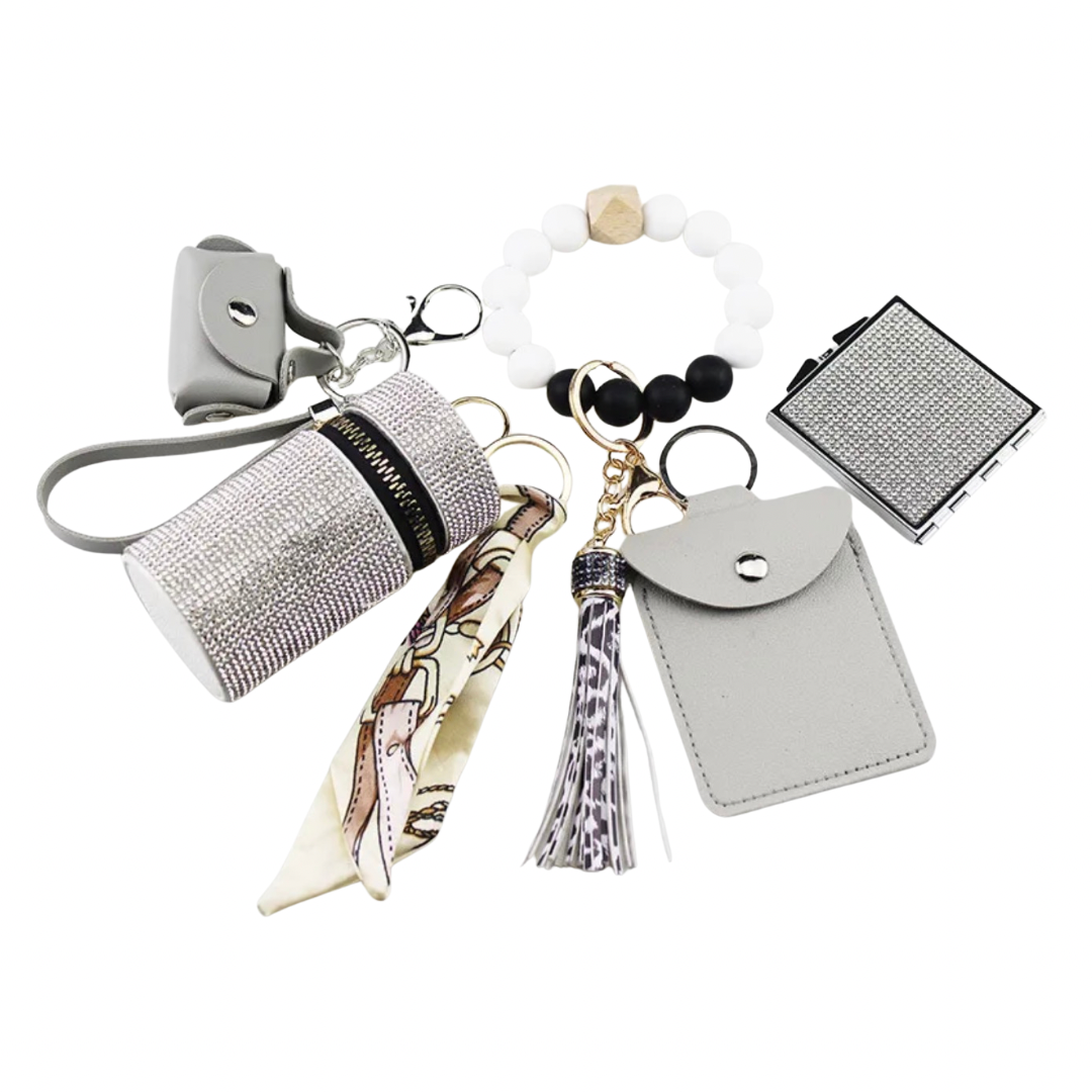 White  Luxe keychain wristlet accessory set featuring a beaded wristlet, rhinestone zip pouch, mini pouch, tassel charm, card holder, and sparkly compact mirror in coordinating colors.