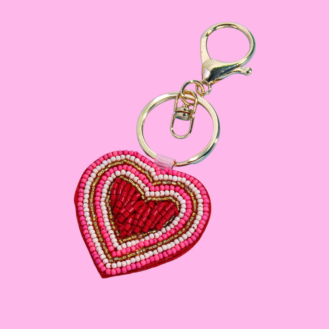 Heart beaded bag charm with red, pink, white, and gold beads in concentric heart pattern, hanging from a gold-tone clasp.